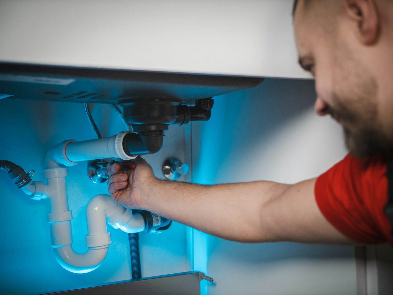 A plumber fitting a drain under a sink.