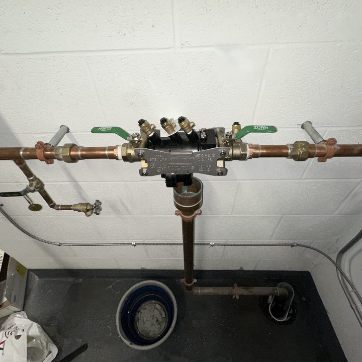 A backflow preventer with green-handled valves on a copper water line.