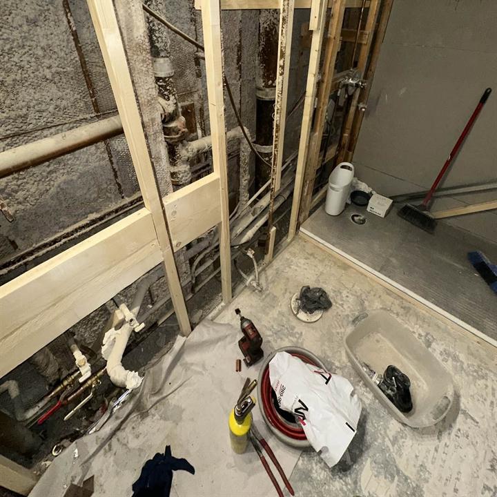 A bathroom stripped to the studs, with new drain and water lines in the floor.