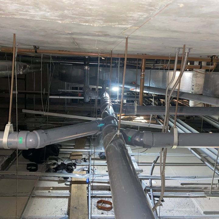 New grey drain lines and copper water piping hung from a concrete ceiling.