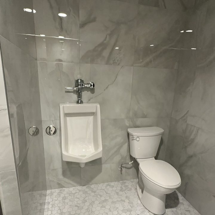 A urinal and toilet installed in a marble-tiled commercial washroom.