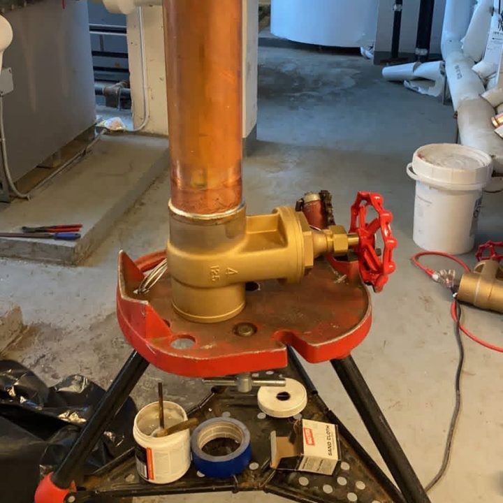A brass gate valve with a red handwheel on copper pipe, set up on a pipe stand.