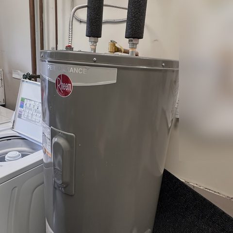 An electric hot water tank with insulated pipes at the top.