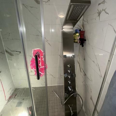 A stainless shower panel installed on a tiled shower wall.