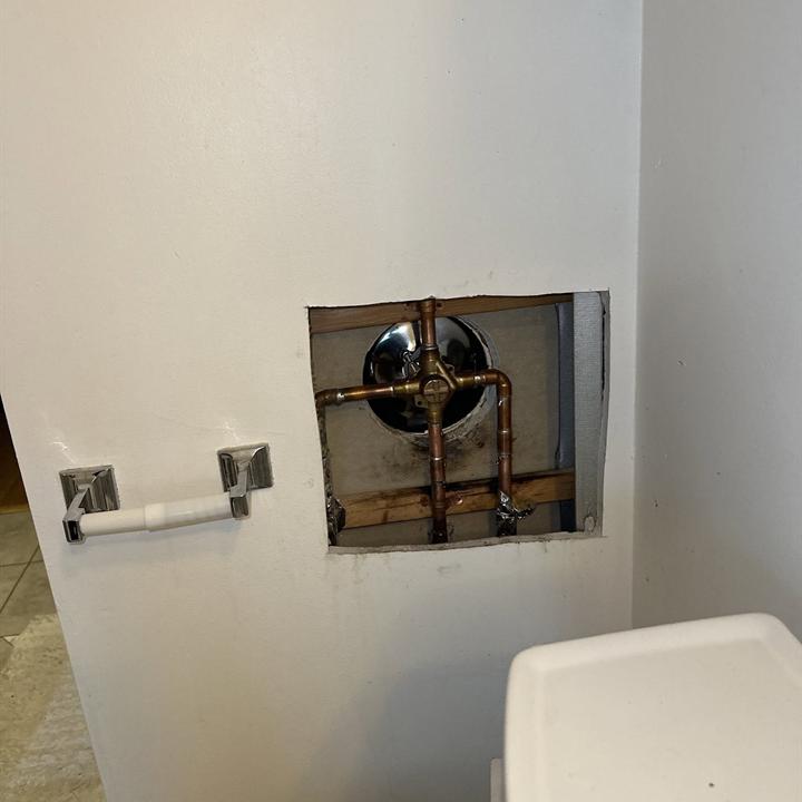 A shower valve behind a square access opening in a finished wall.