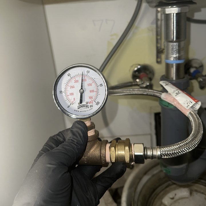 A pressure gauge connected to a water line under a sink during a pressure test.